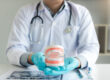 Dentist holding dentures in office room.